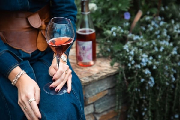 Woman sitting in an autumn garden holding a glass of rosé champagne, seasonal foliage around her, bottle nearby.