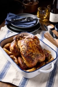 Golden roast chicken presented on a serving platter at a beautifully styled table set for an intimate dinner.