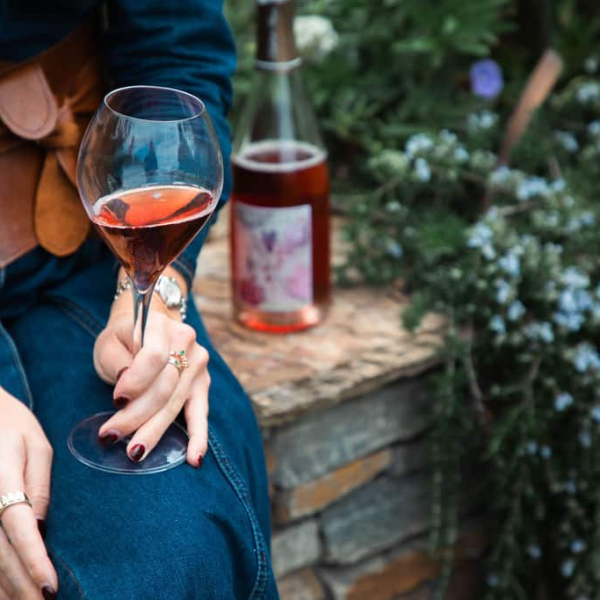 Woman sitting in an autumn garden holding a glass of rosé champagne, seasonal foliage around her, bottle nearby.
